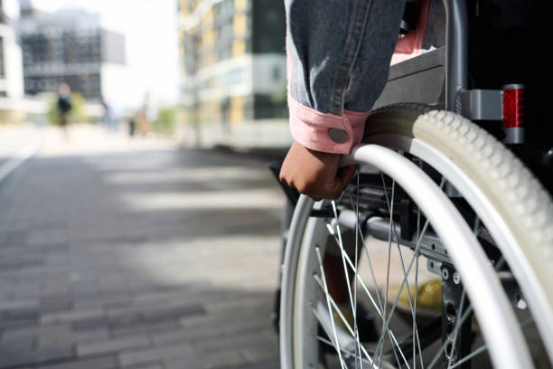 A woman's hand grips the wheel of a wheelchair as she travels down a sidewalk.